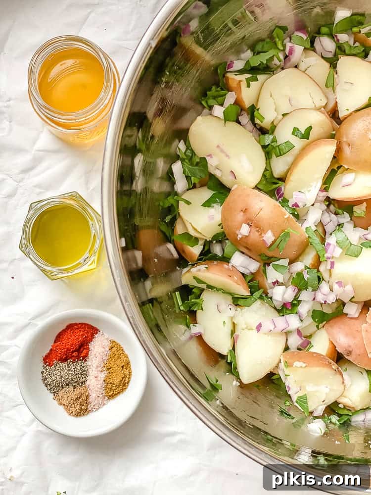 Process shot showing spices, oil, and vinegar in jars next to a bowl of French potato salad.