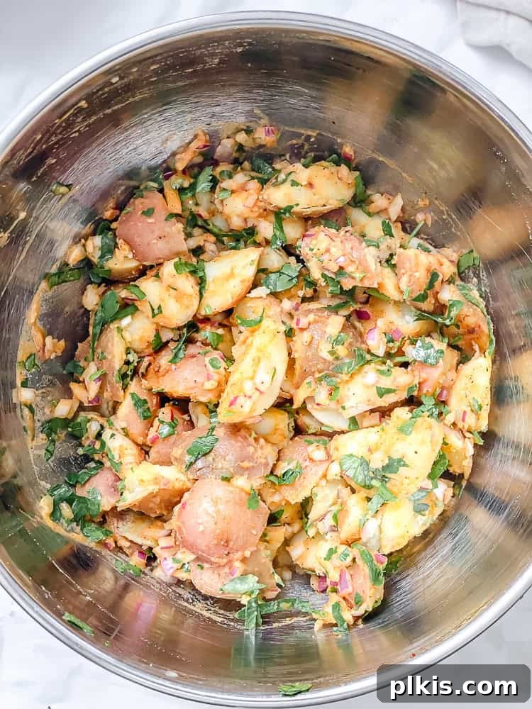 Process shot showing French potato salad in a metal bowl, fully dressed and ready to absorb flavors.
