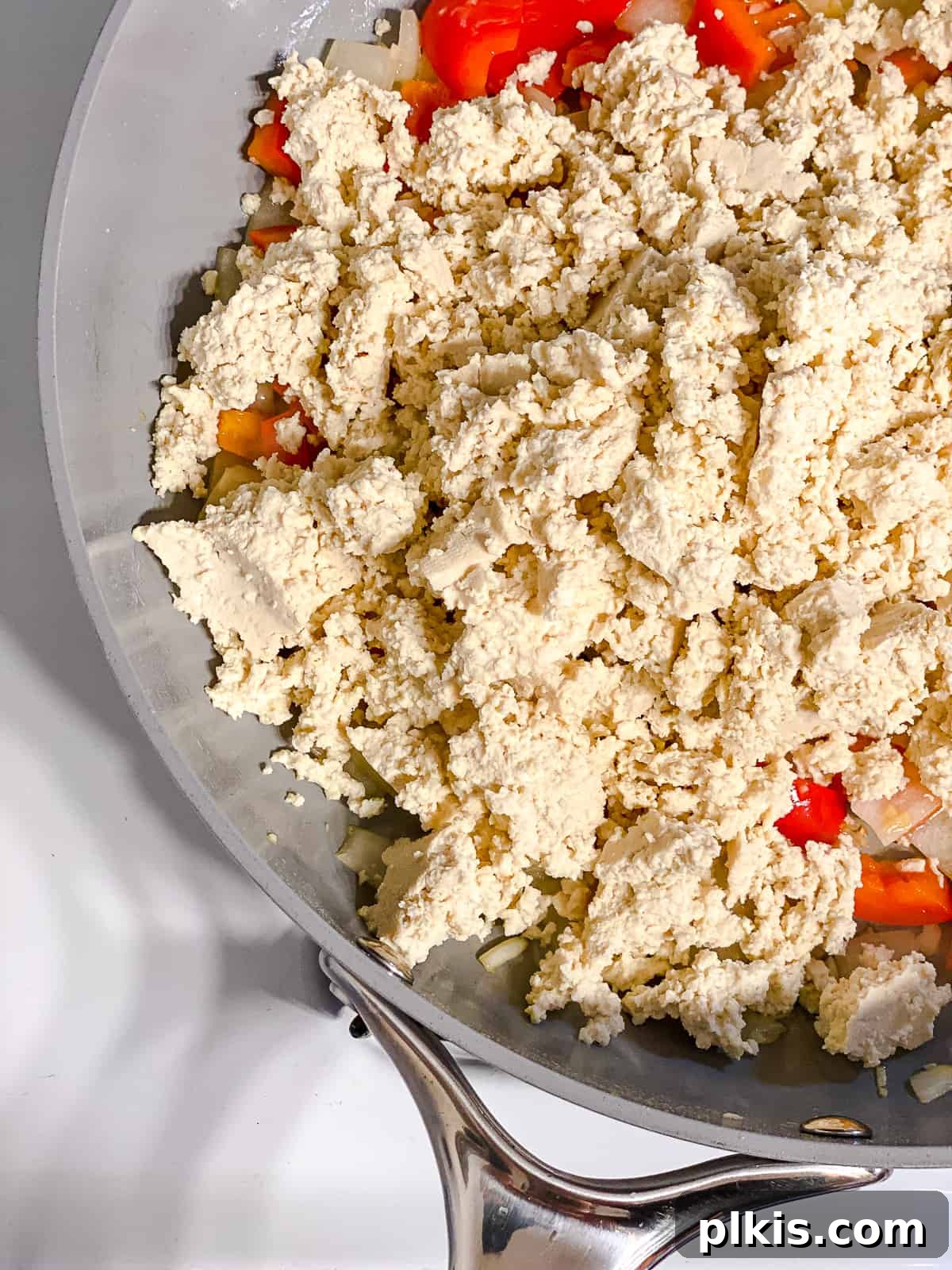 Fluffy and Flavorful Vegan Tofu Scramble with Garden Veggies 6 Process shot of crumbling firm tofu into the skillet with sautéed vegetables.