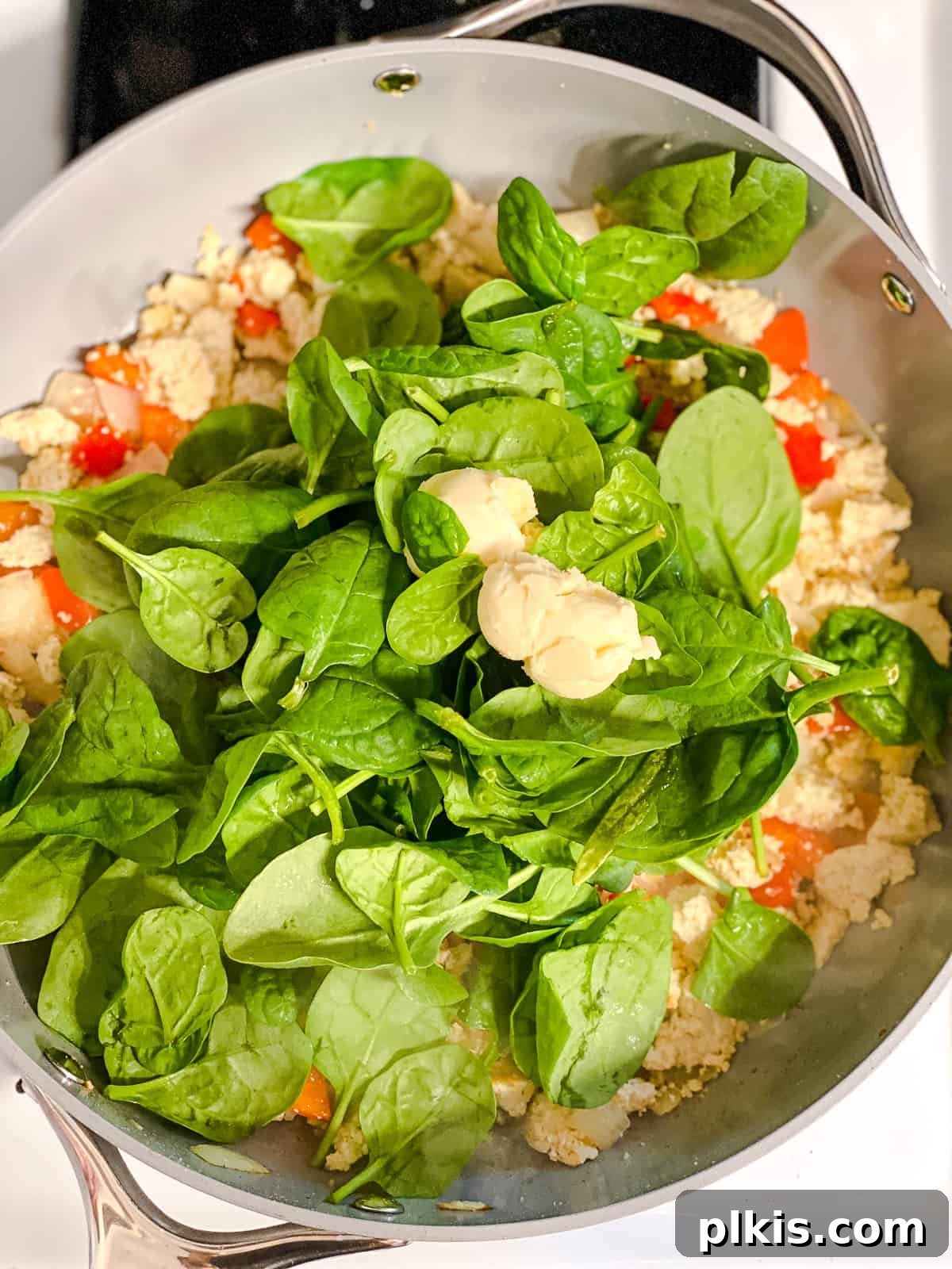 Fluffy and Flavorful Vegan Tofu Scramble with Garden Veggies 7 Process shot of adding fresh spinach and vegan butter to the tofu scramble in the pan.