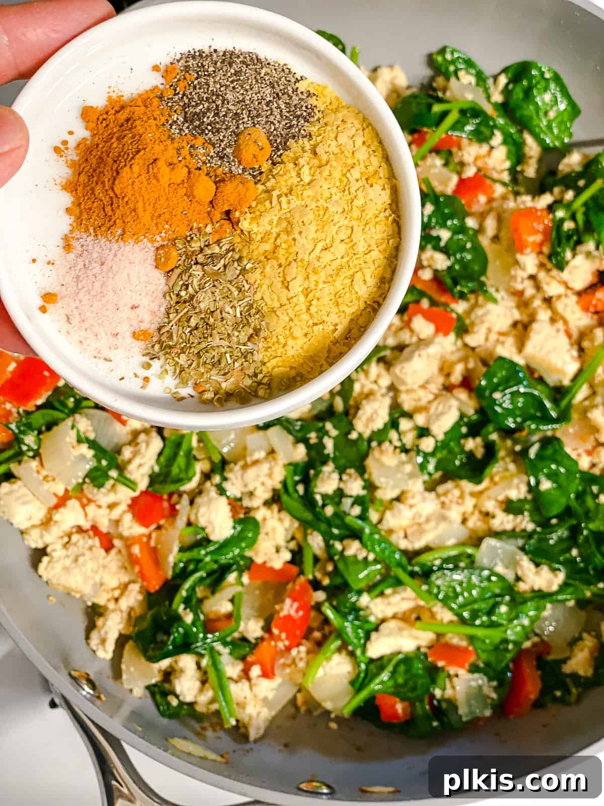 Fluffy and Flavorful Vegan Tofu Scramble with Garden Veggies 8 Process shot of adding turmeric and other spices to the tofu and vegetable mixture in the pan.