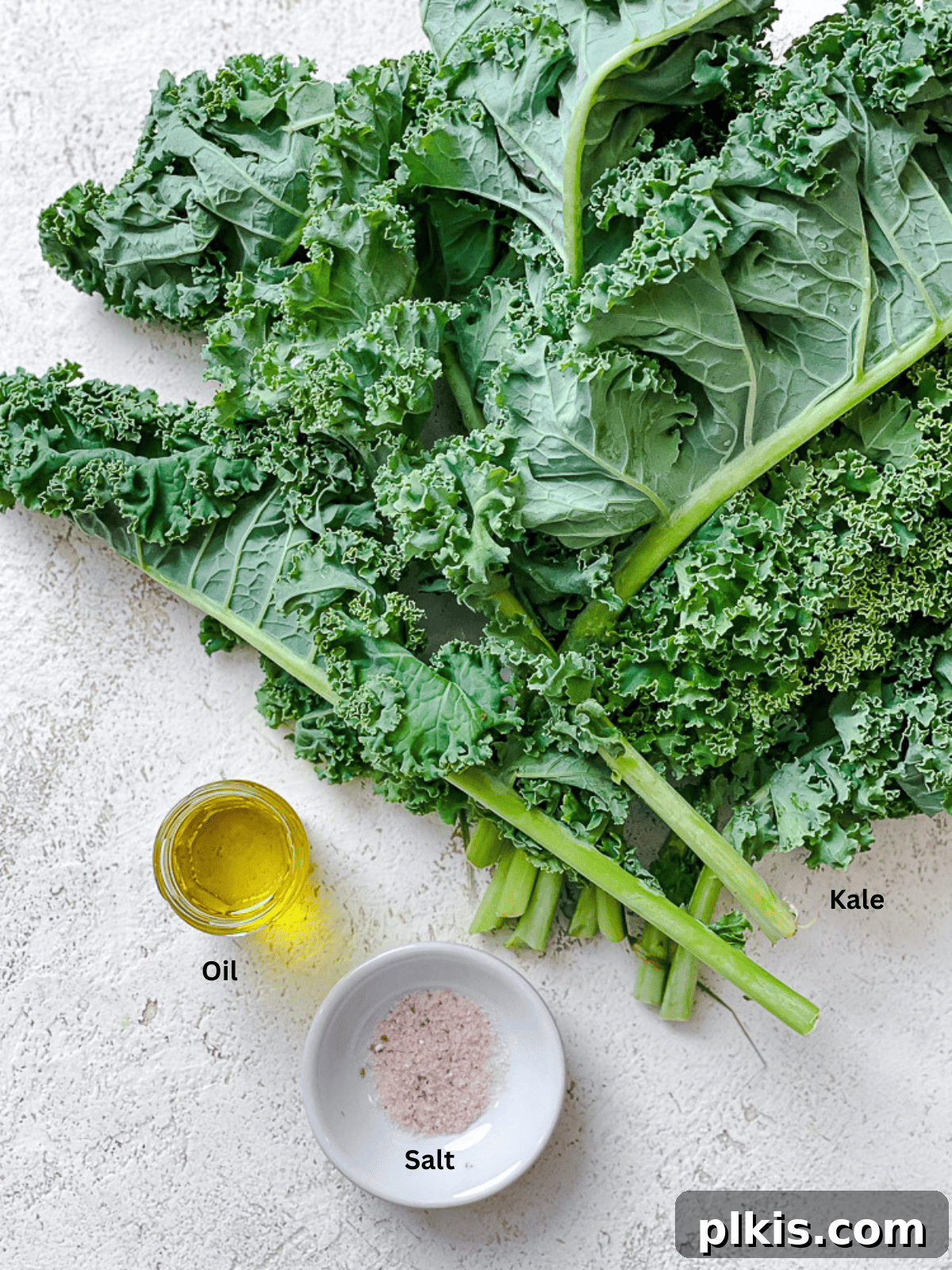 Ingredients for Crispy Baked Kale Chips laid out on a white surface, including kale, oil, and salt.