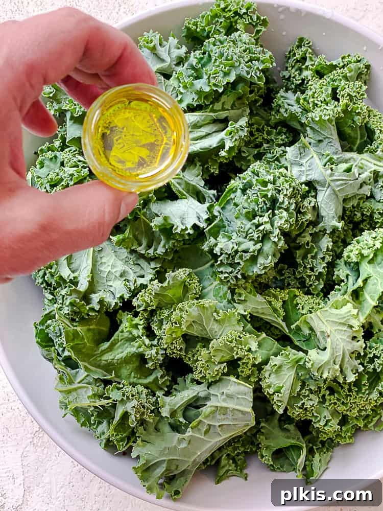 Process shot of adding oil to kale in a large bowl.