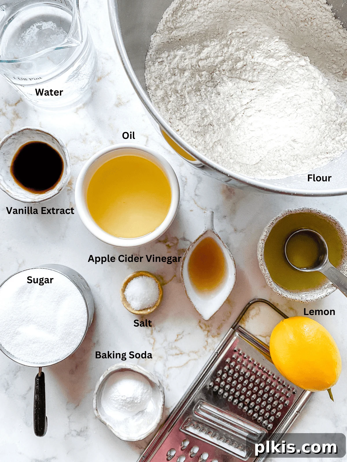 Bright & Tangy Vegan Lemon Loaf 3 A collection of ingredients for a lemon loaf cake, neatly measured out in bowls and placed on a pristine white surface, ready for mixing.