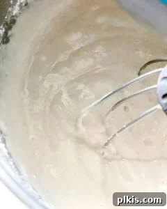 Bright & Tangy Vegan Lemon Loaf 5 Close-up view of a mixing bowl with an electric mixer actively combining ingredients to form a smooth lemon loaf batter.