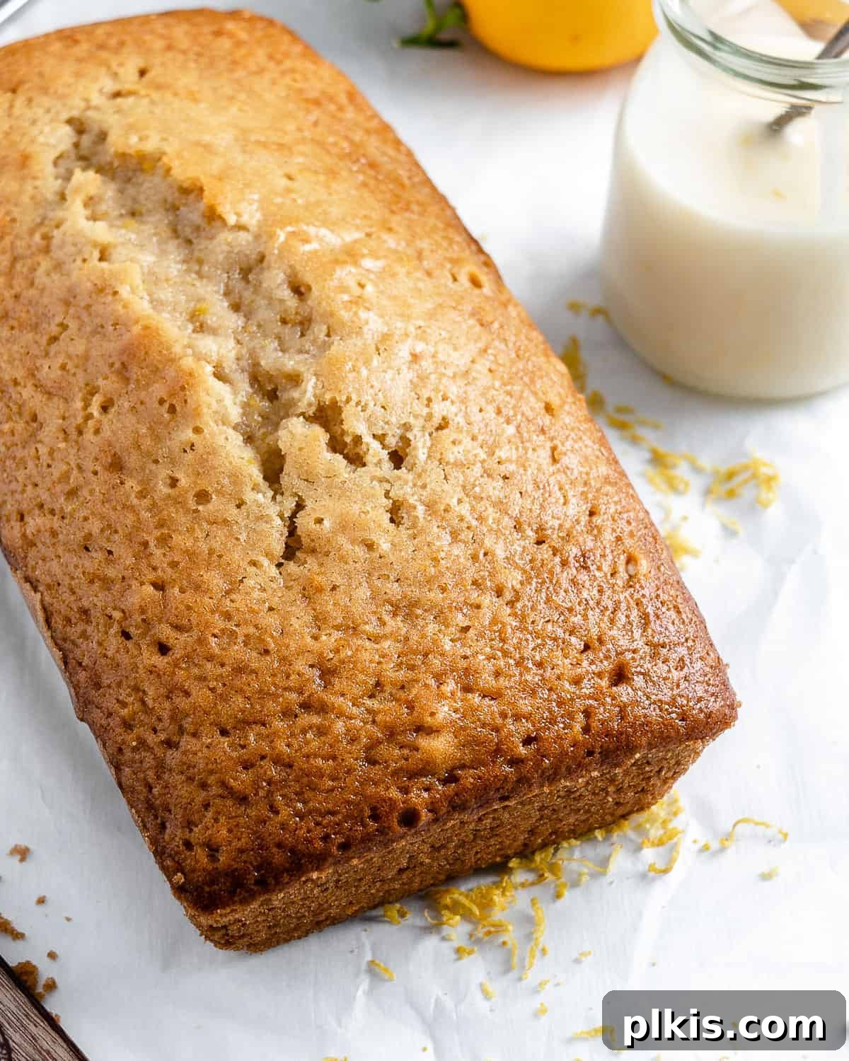 Bright & Tangy Vegan Lemon Loaf 9 A vibrant, sunny vegan lemon loaf cake, beautifully glazed and garnished with fresh lemon zest, sitting on a white background.