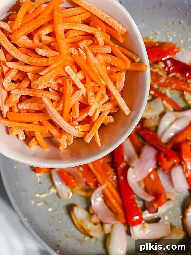 Yaki Udon Stir Fry 6 Process shot showing sliced onions and bell peppers being added to a hot pan for sautéing.