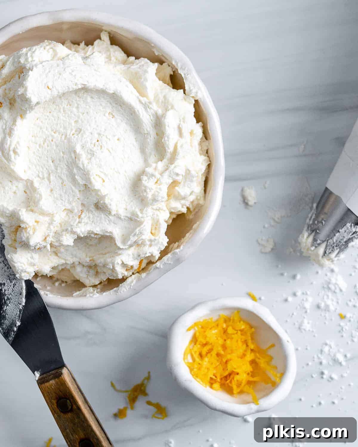 Luscious Vegan Lemon Buttercream 7 A pristine white bowl filled with finished vegan lemon buttercream frosting, placed on a clean white background, with fresh lemon zest sprinkled delicately in the background, highlighting the key flavor.