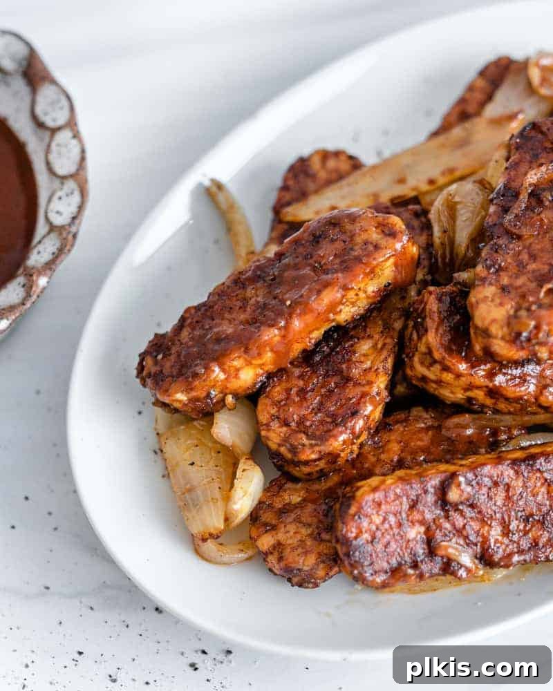 Sweet & Smoky Tempeh BBQ 15 Completed BBQ Tempeh plated on a white plate with BBQ sauce on the side