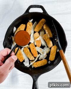 The process of adding BBQ sauce to a pot with tempeh and onion