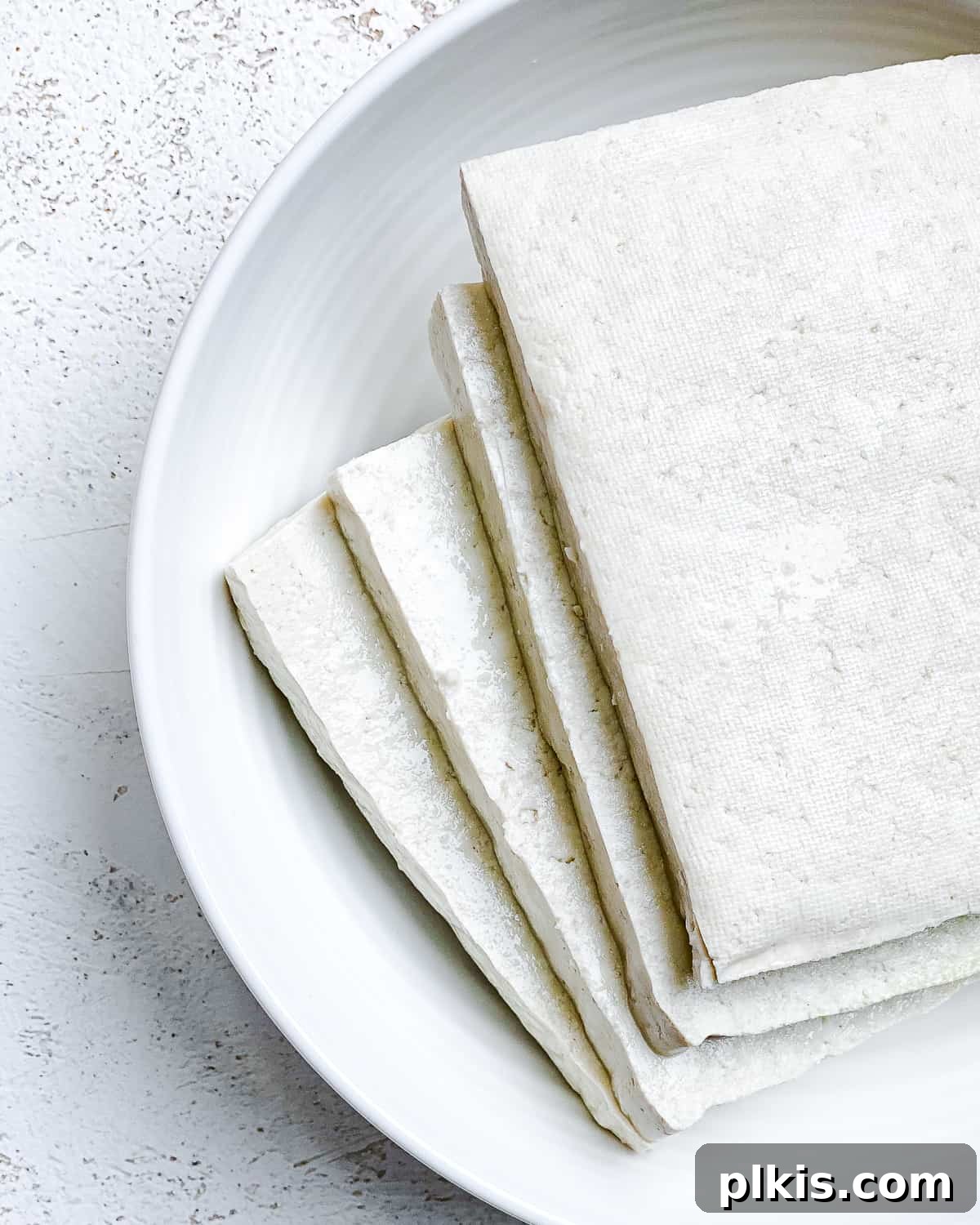 Four evenly sliced pieces of tofu are neatly arranged on a clean white plate, ready for the next stage of preparation in making the Easy Crispy Buffalo Tofu Sandwich.