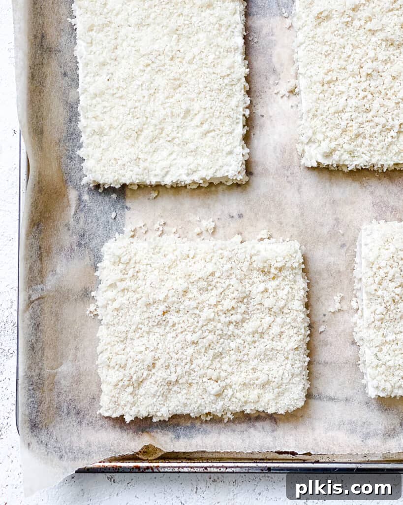 A process shot showing breaded tofu slices carefully arranged on a baking sheet, ready for the oven to become crispy buffalo tofu patties.