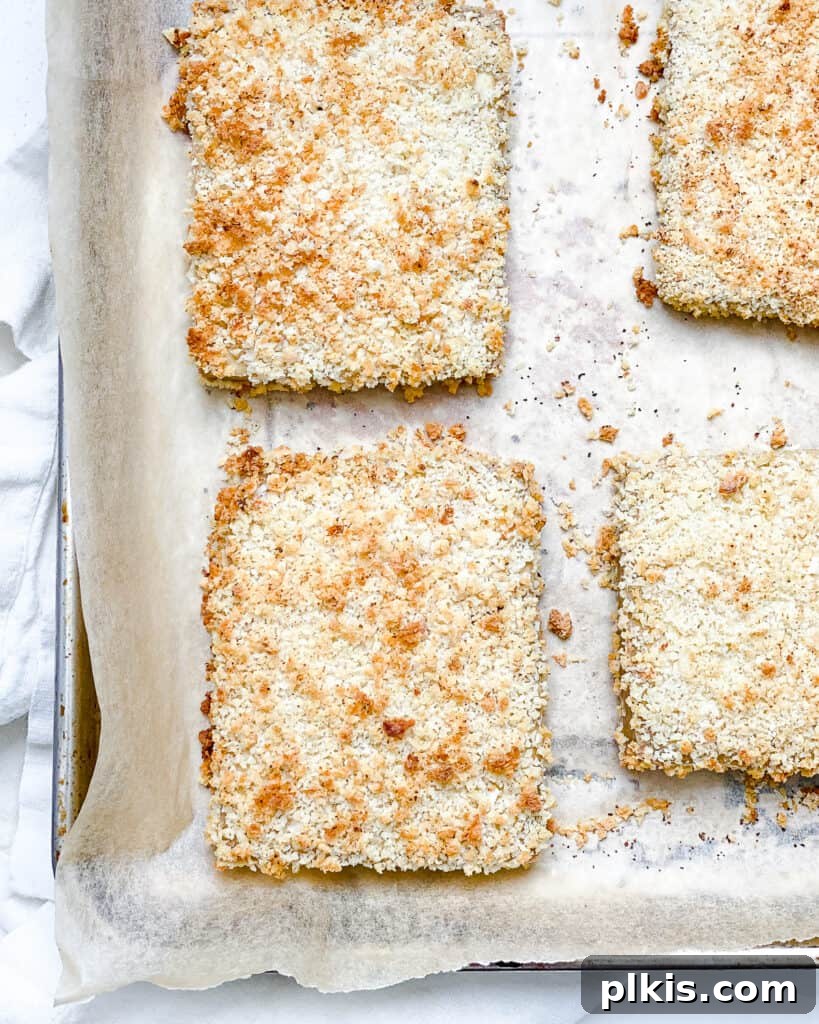 Another process shot, this one capturing the moment additional bread crumbs are being pressed onto the tofu slices on the baking sheet, ensuring full coverage and maximum crispness for the Easy Crispy Buffalo Tofu Sandwich.