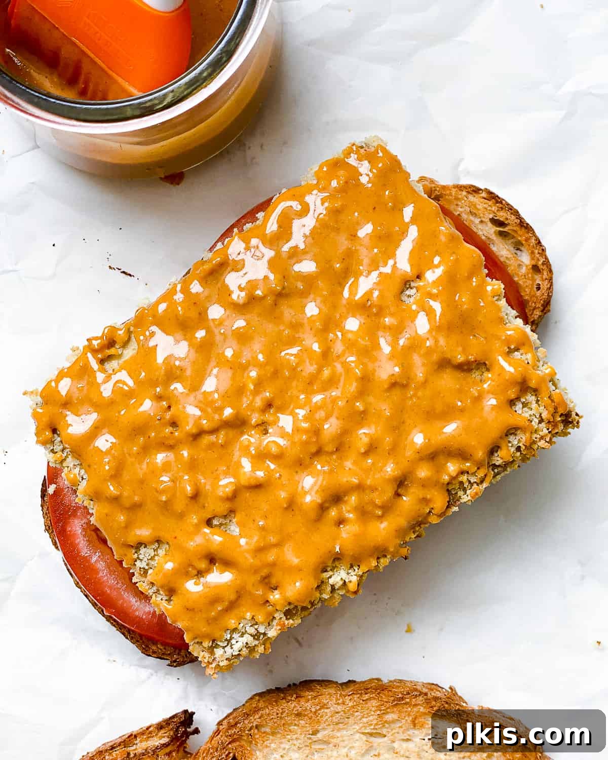 A process shot showing a buffalo tofu slice being carefully placed onto the bottom half of a bread slice, marking the beginning of the sandwich assembly for the Easy Crispy Buffalo Tofu Sandwich.
