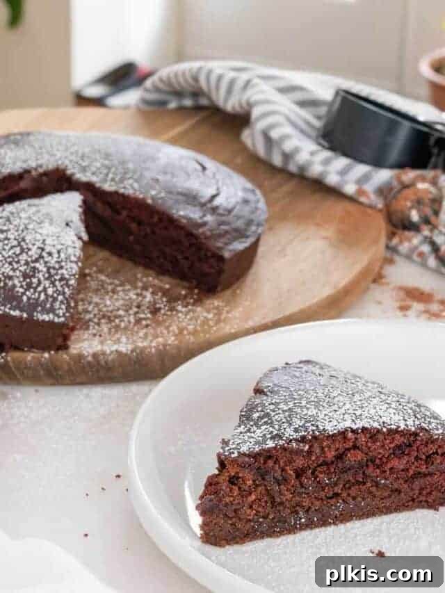 35 Irresistible Vegan Cake Creations 10 A decadent chocolate crazy cake with a perfectly cut slice placed on a white plate in the foreground, and the full cake in the background on a brown platter.