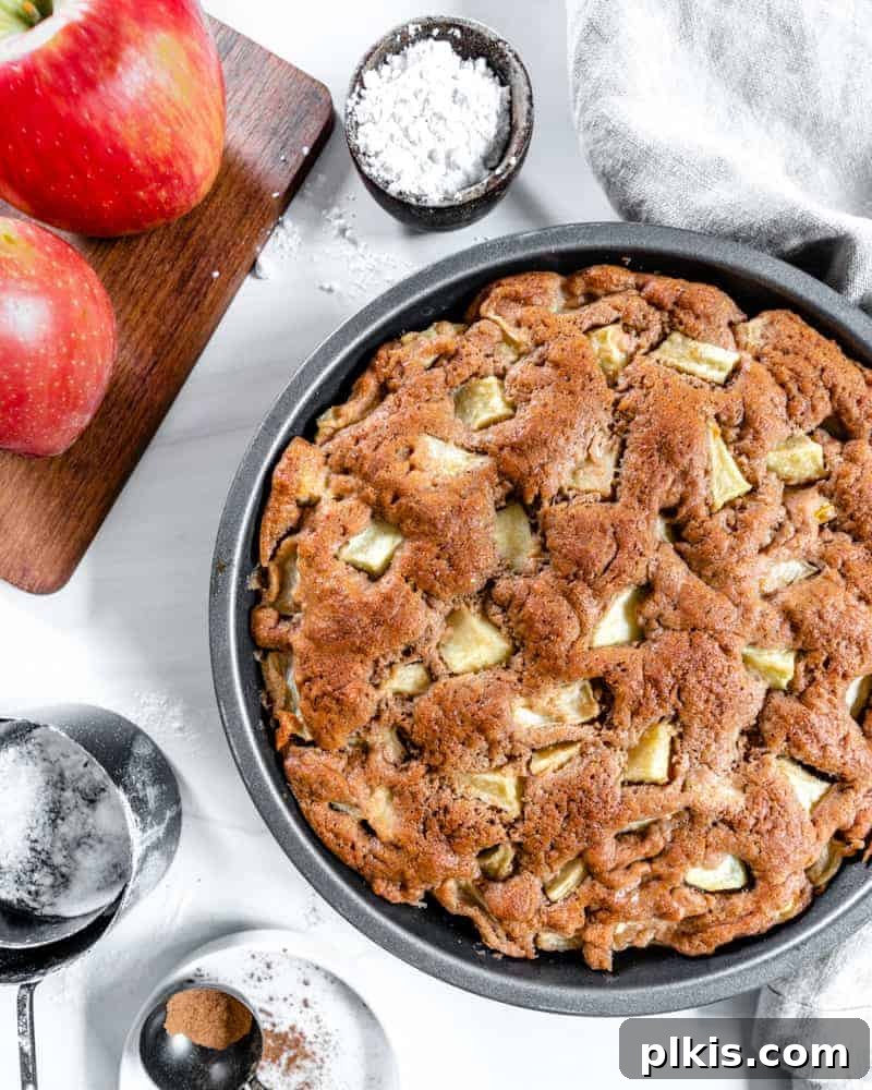 35 Irresistible Vegan Cake Creations 24 A beautifully baked vegan apple cake, presented alongside two fresh apples and measuring tools, all set against a clean white background.