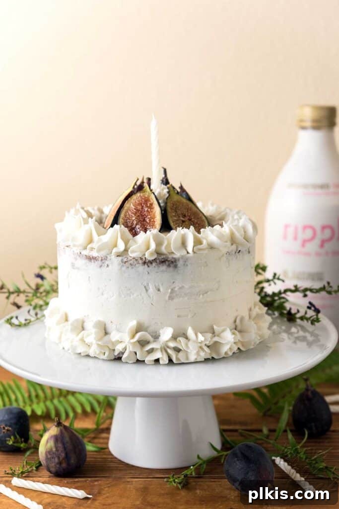 35 Irresistible Vegan Cake Creations 31 A stunning vegan fig cake, elegantly presented on a white cake platter, against a light background, with a carton of plant-based milk in the distance.