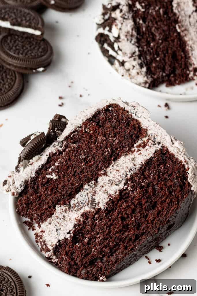 35 Irresistible Vegan Cake Creations 35 A rich slice of vegan Oreo cake, revealing its chocolate layers and creamy Oreo buttercream, presented on a white plate with the full cake in the background.