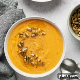 completed pumpkin soup in two bowls against a white background with spoons and a gray towel in the background