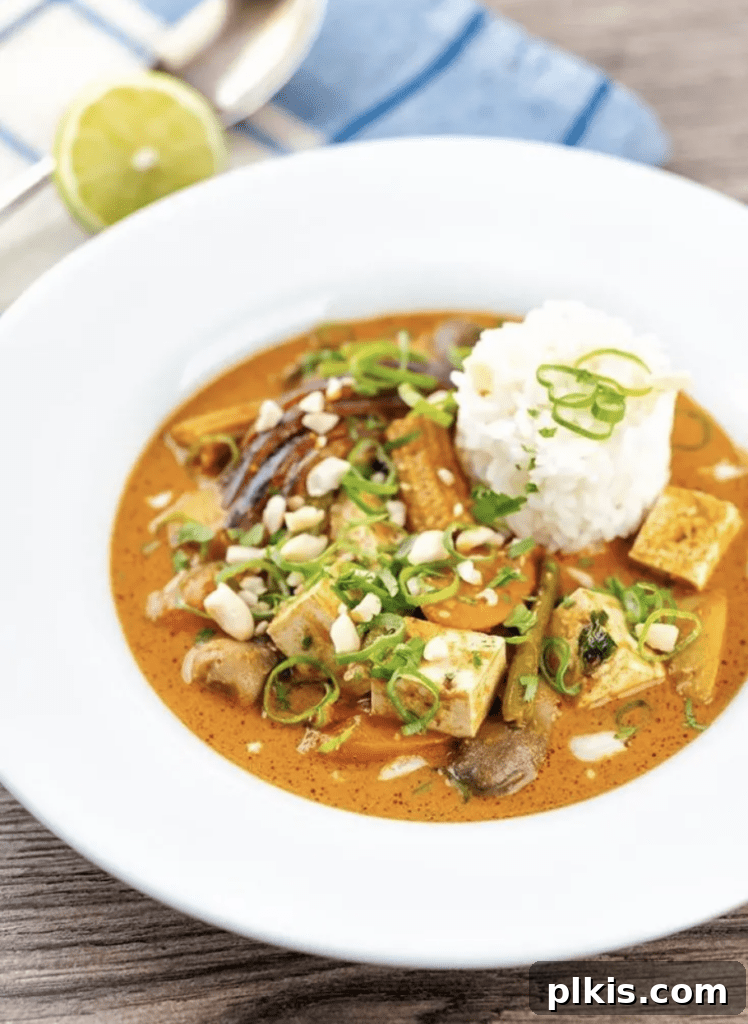 Over 30 Quick and Flavorful Vegan Instant Pot Recipes 22 completed Thai Massaman Curry in a white bowl against a wood surface with a blue towel in the background