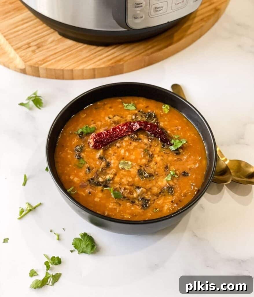 Over 30 Quick and Flavorful Vegan Instant Pot Recipes 25 completed Dal Tadka Instant Pot Recipe in a small black bowl against a white background with herbs scattered against the surface