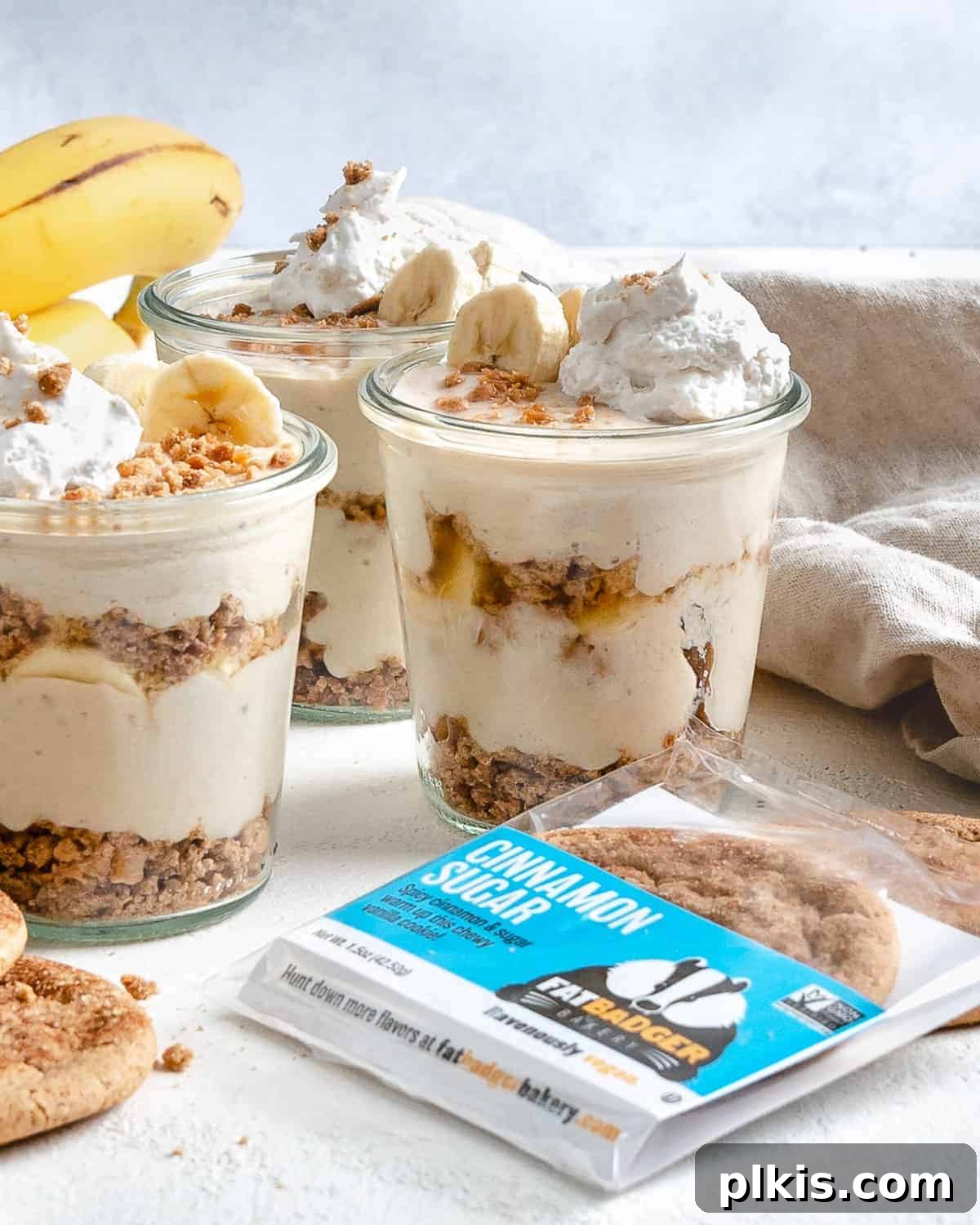 Layered Banana Dream 2 Several completed vegan banana parfaits in glass jars with a cookie in the forefront, showcasing the layers