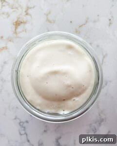 Layered Banana Dream 10 Process of banana cream mixture on top of granola in a glass container against a white marble background