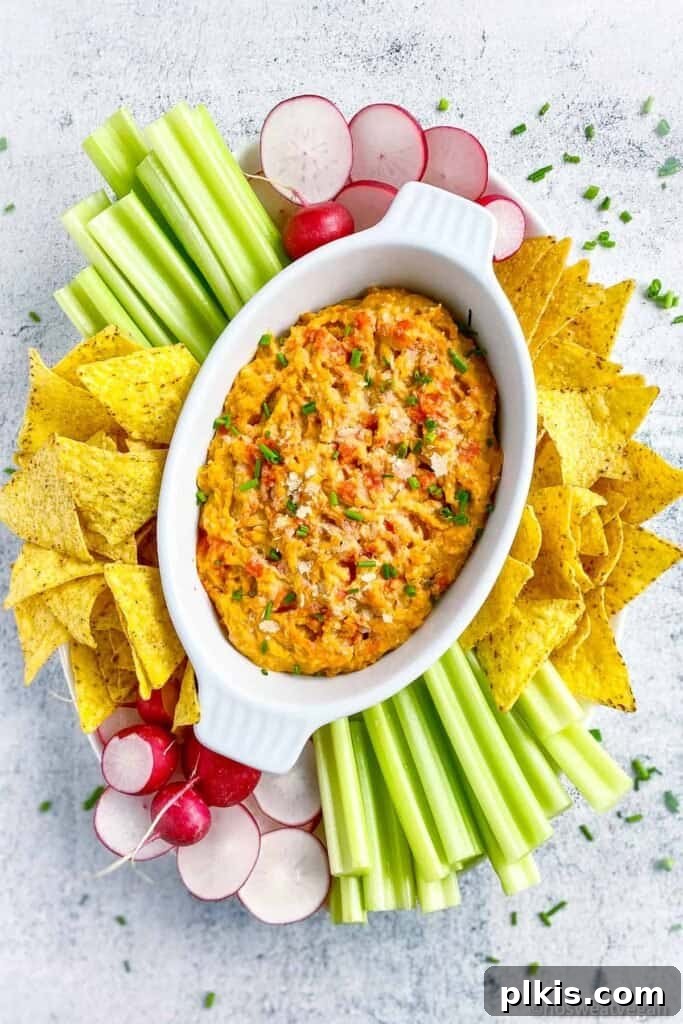 50 Quick Vegan Bites 18 A completed buffalo chickpea dip in a white platter, elegantly surrounded by chips and fresh veggies against a clean white background.