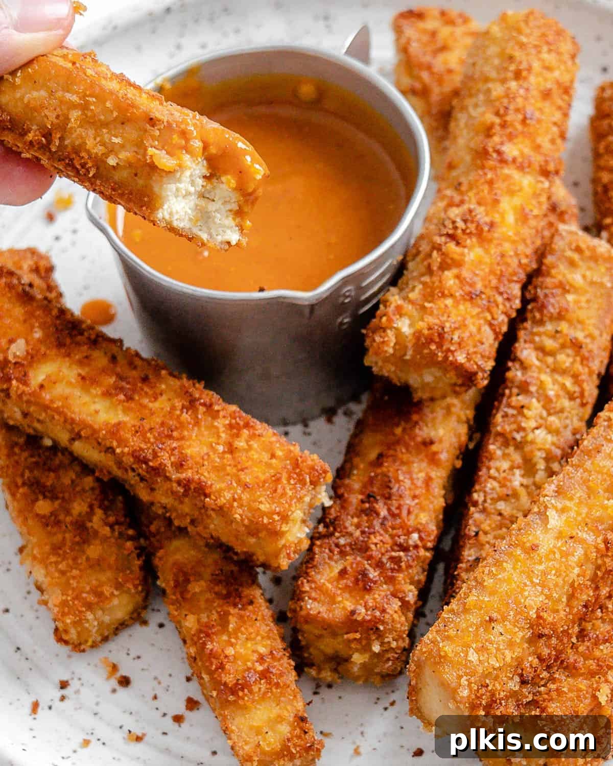 50 Quick Vegan Bites 31 Completed vegan breaded tofu strips artfully arranged on a white plate with a small bowl of dipping sauce.