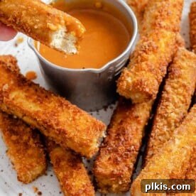 completed vegan breaded tofu strips on a white plate with a small bowl of sauce on the plate