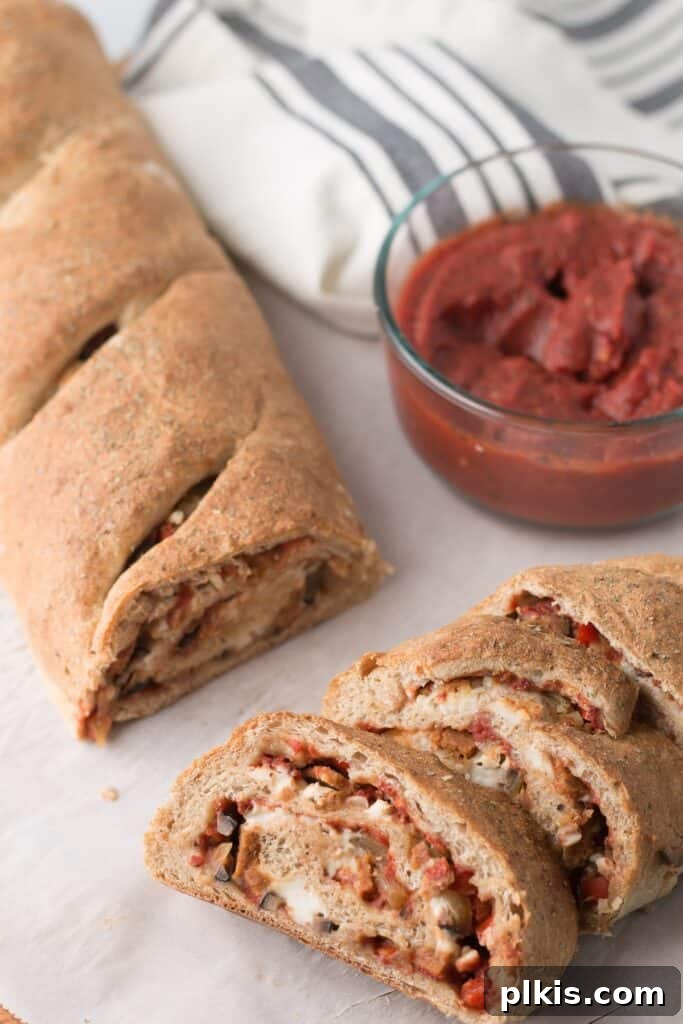 50 Quick Vegan Bites 38 A completed Vegan Stromboli, with one slice visible in the foreground and a delicious sauce blurred in the background.