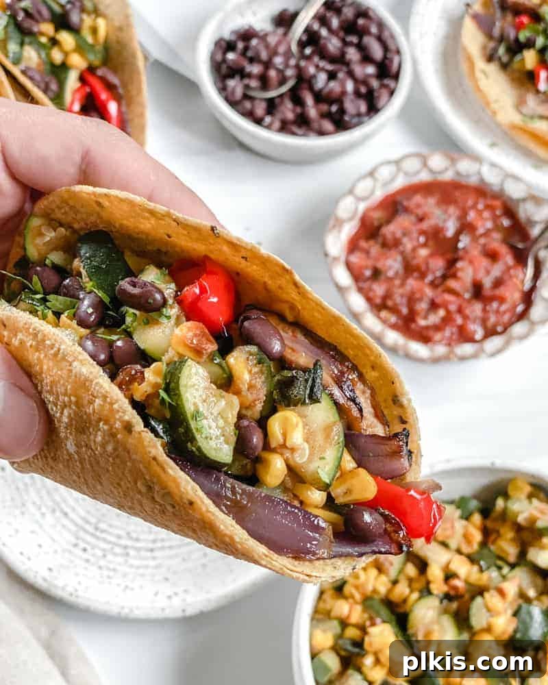 50 Quick Vegan Bites 46 Vegan Roasted Veggie Tacos served on a white plate with fresh ingredients in the background against a white surface.