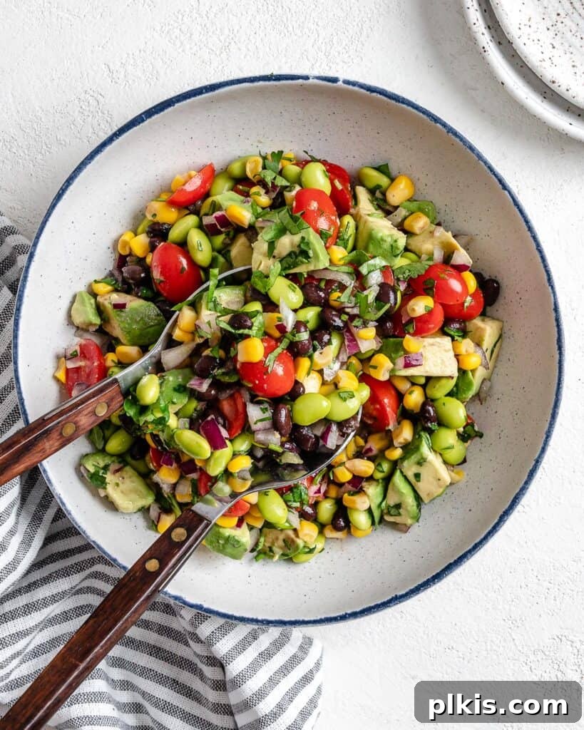50 Quick Vegan Bites 64 A completed white bowl of Easy Edamame Salad with utensils gracefully placed in the bowl against a clean white background.