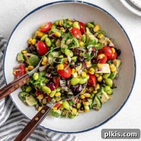 completed white bowl of Easy Edamame Salad with utensils in bowl against a white background
