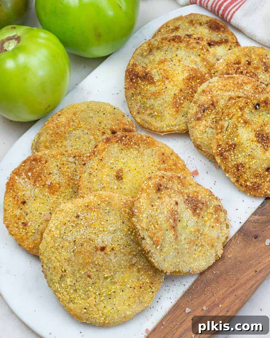 Vegan Fried Green Tomatoes Several perfectly fried green tomato slices piled on a white background, with scattered fresh green tomatoes.