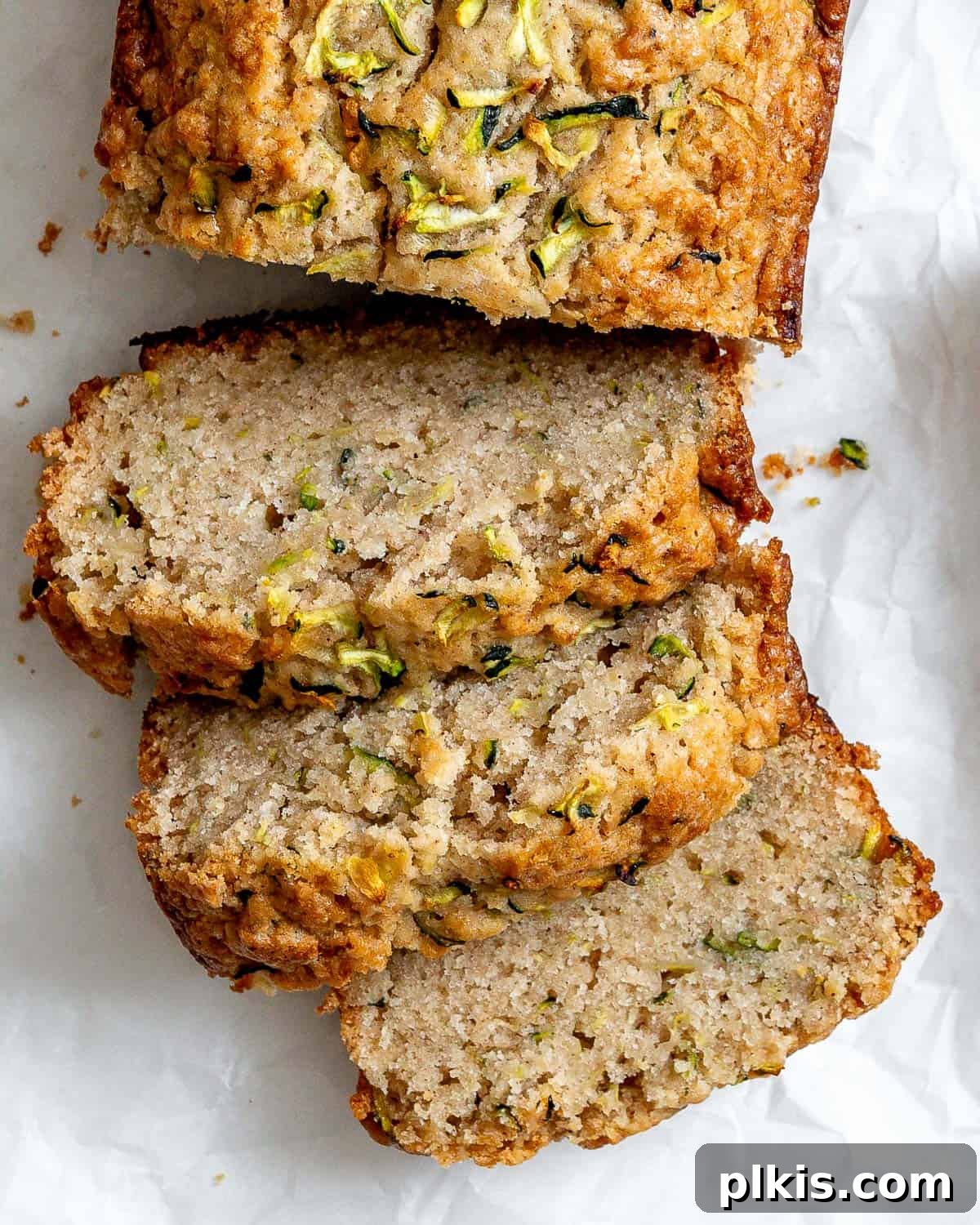 Slices of perfectly baked vegan zucchini bread arranged on white crinkled parchment paper, invitingly soft and moist.