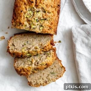 Slices of zucchini bread on white crinkled parchment paper, next to a speckled bowl and gray napkin.