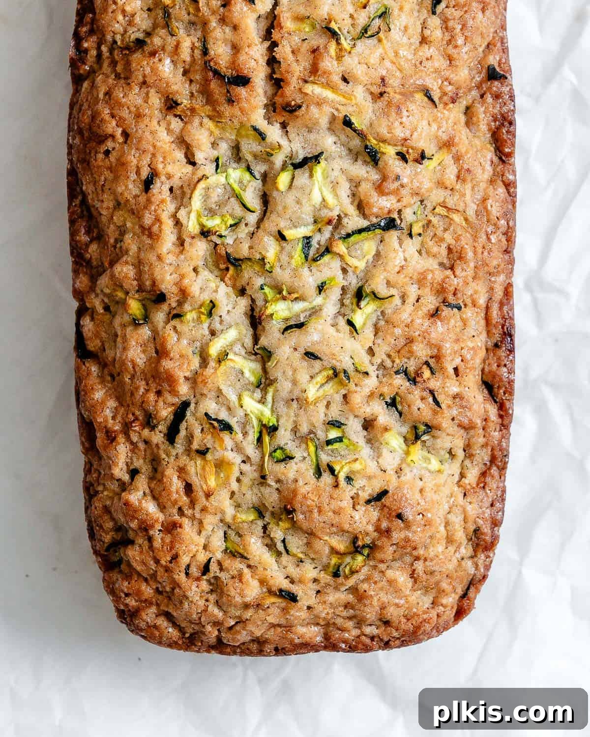 A freshly baked, golden-brown loaf of zucchini bread cooling on white crinkled parchment paper.