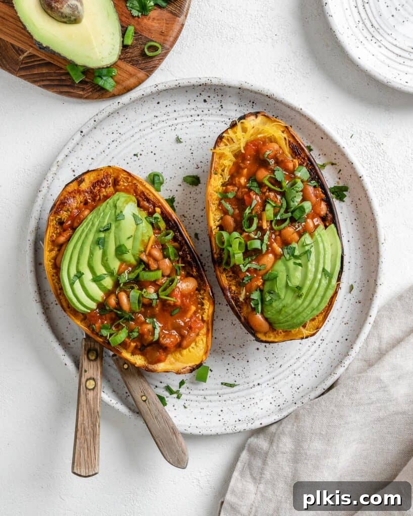 Golden Spaghetti Squash Bowls with Spicy Chili Cheese 2 Completed chili cheese stuffed spaghetti squash in a white plate, garnished with fresh herbs and avocado.