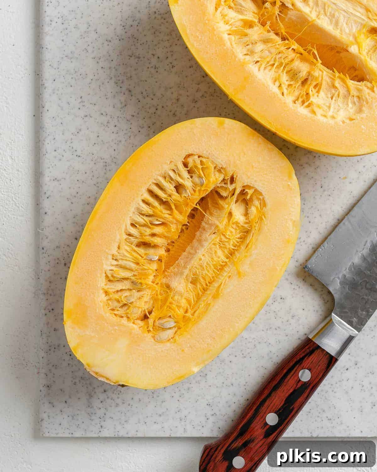 Golden Spaghetti Squash Bowls with Spicy Chili Cheese 4 Spaghetti squash cut in half on a white speckled cutting board, seeds removed.