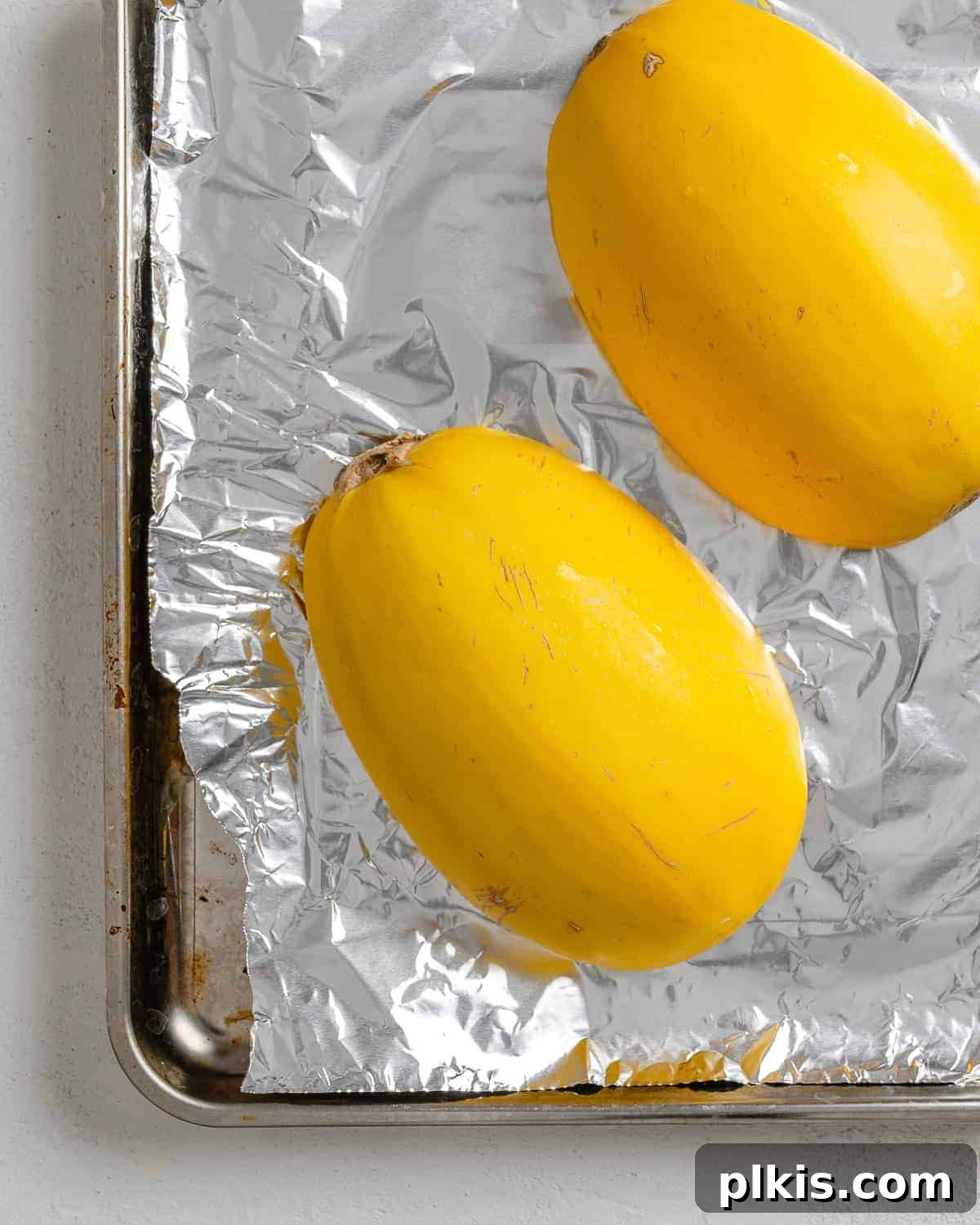 Golden Spaghetti Squash Bowls with Spicy Chili Cheese 5 Halved spaghetti squash placed cut-side down on aluminum foil in a baking tray, ready for the oven.