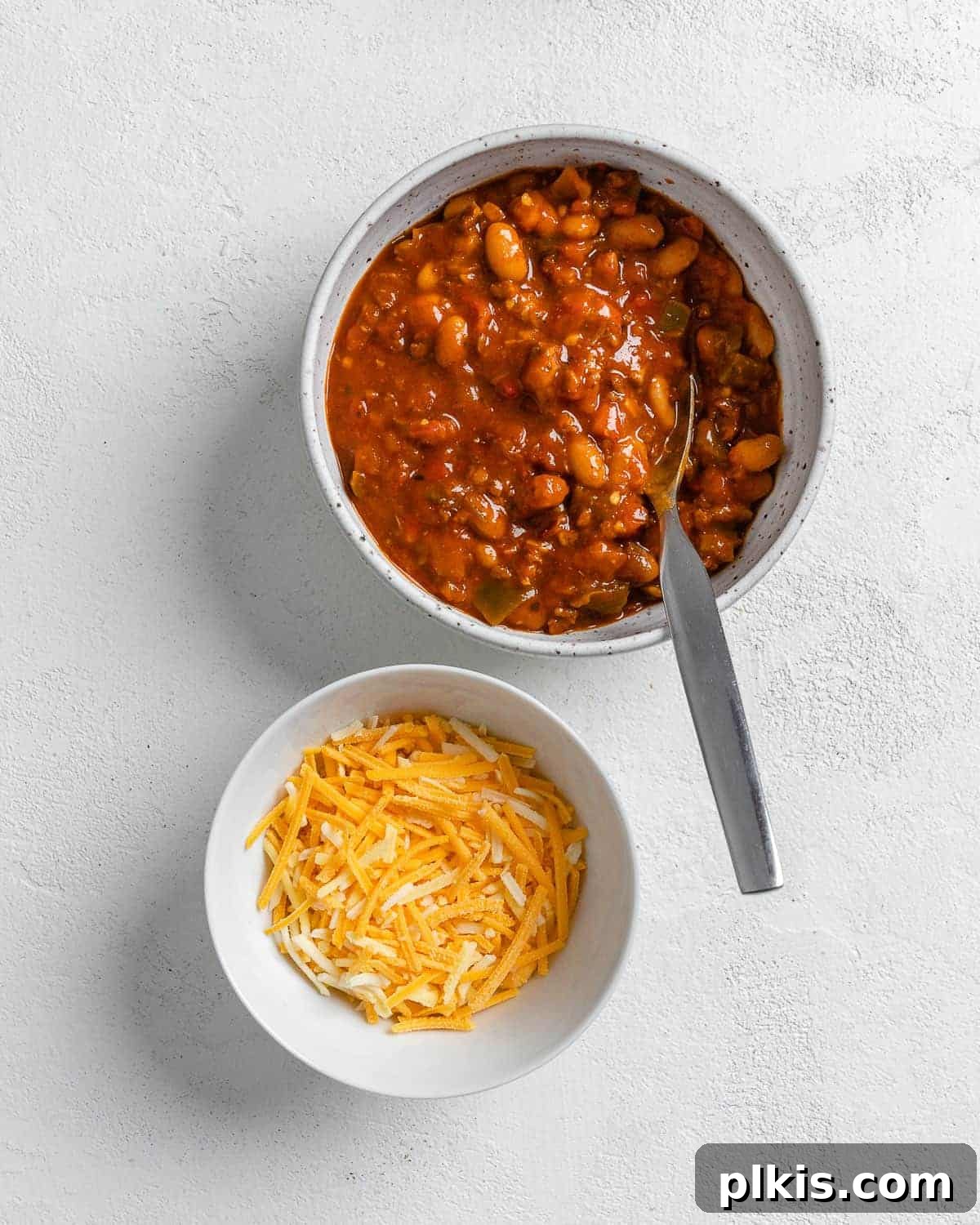 Golden Spaghetti Squash Bowls with Spicy Chili Cheese 7 Vegan cheese being stirred into a bowl of Blount's Plant-Based Chili, on a white surface.