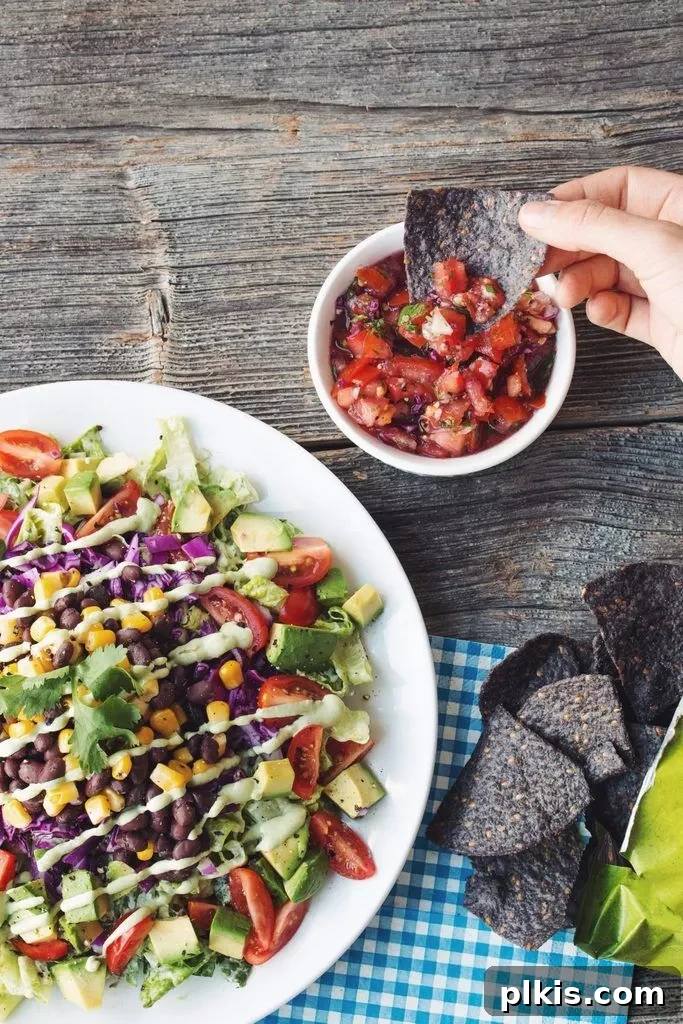 Quick & Delicious: 30-Minute Vegan Dinners 37 Completed Fully Loaded Taco Salad in a white plate with salsa in a small bowl against a wood background.