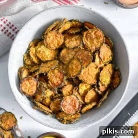 Crispy dehydrator vegan cheesy zucchini chips in a white bowl, with more chips in the background.