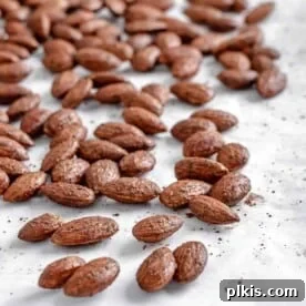 A scattering of golden-brown cinnamon almonds on a white surface.