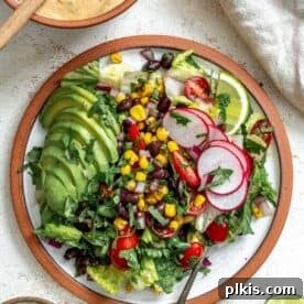 A vibrant vegan taco salad in a tortilla bowl, topped with avocado, radishes, and lime wedges.
