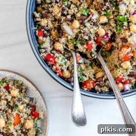 A blue bowl filled with a fresh quinoa salad and serving utensils.