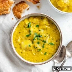 A white bowl of Lentil Potato Soup, with fresh ingredients in the background.