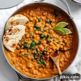A large skillet filled with curried chickpeas, served with vegan naan.