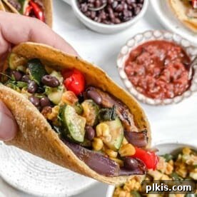 Vegan Roasted Veggie Tacos arranged on a white plate with fresh ingredients in the background.